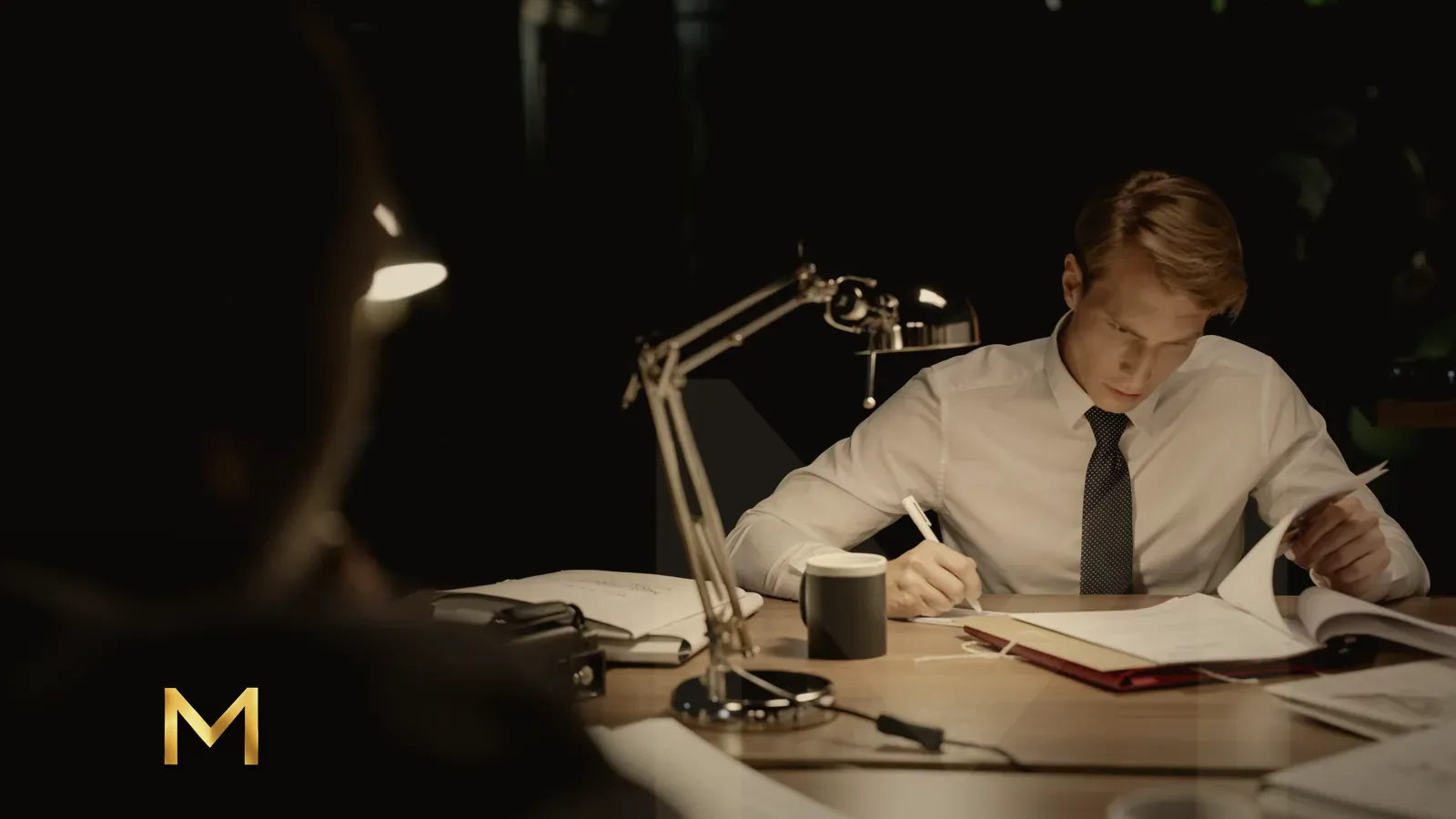 A man working through paperwork under a desk lamp at night
