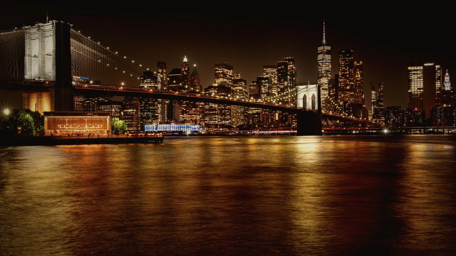 The Brooklyn Bridge and the Manhattan skyline lit up at night above the East River